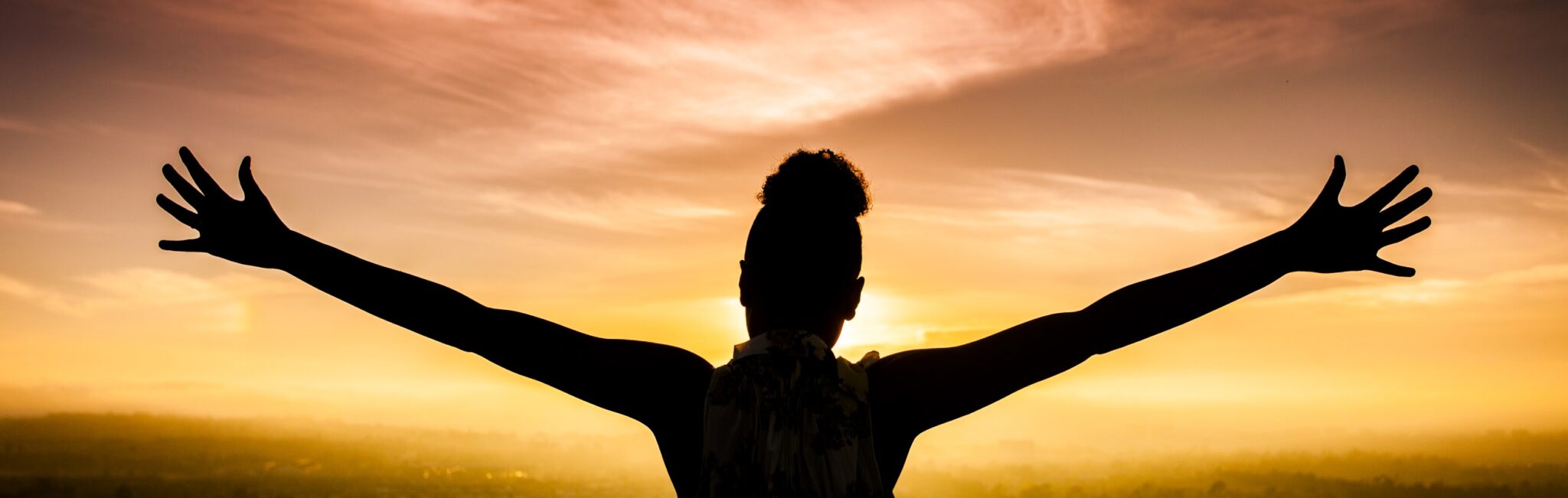 Woman with her arms open wide with joy facing the sunset.